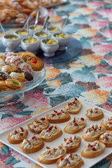 Breakfast table with Galician desserts and appetizers, tea pastries, carnival ears, small cups of fresh fruit, colorful tablecloth, hydrangeas