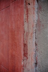 Close up of a red painted wall with visible cracks and deterioration, highlighting the effects of time and weather
