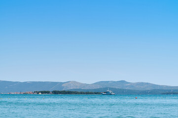 Fototapeta premium Bright blue sky above serene waters with small boat near an island on a sunny day, showcasing coastal beauty.