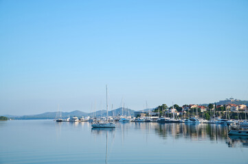 Fototapeta premium Sailboats are anchored peacefully in a serene harbor against a backdrop of distant hills and clear blue sky.