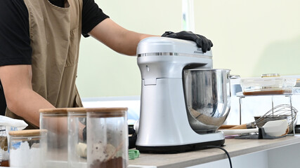 A person is making a cake in a kitchen. The person is wearing a black apron and gloves. The cake...
