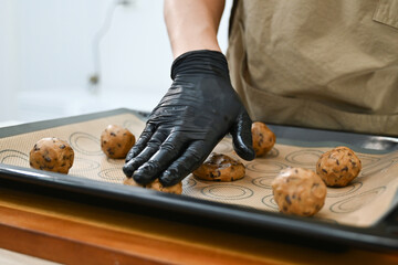 A man is making cookies and wearing gloves. He is using a scale to measure the ingredients. The cookies are on a baking sheet.