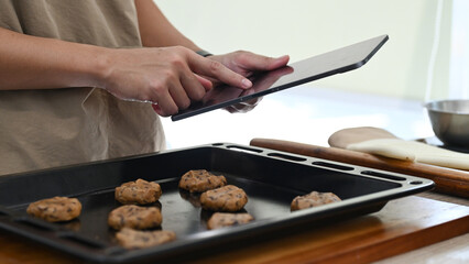A man is cooking in a kitchen while holding a tablet. He is using the tablet to look up a recipe or to follow a cooking tutorial.