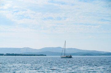 Naklejka premium A sailboat moves gracefully on calm waters surrounded by elegant mountains and a bright sky.