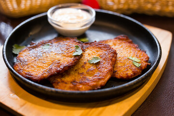 Fried grated potato pancakes with sour cream on frying pan