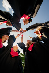 Low ange view vertical photo of groupmates students raise touch diplomas mortarboard gown graduate...