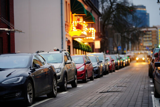 Row of parked cars filling every available roadside space, urban parking difficulties. Parked cars along busy city sidewalk in the evening, limited parking space. Struggle to find vacant spaces