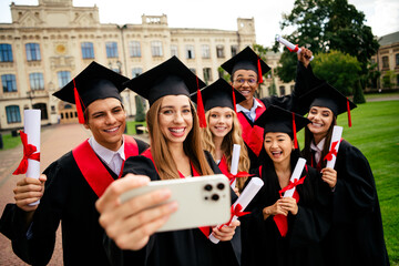 Joyful graduates celebrating their achievement outdoors in a campus setting on a sunny summer day