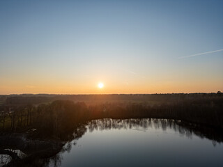 A tranquil and serene sunset beautifully reflects on a peaceful lake that is surrounded by lush greenery and tall trees