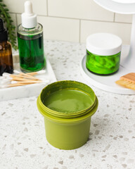 Skincare products and mirror with LED light on marble bathroom table top, tile wall. Cream jar, clay mask, lotion and serum brown bottles on dressing table. Green plants