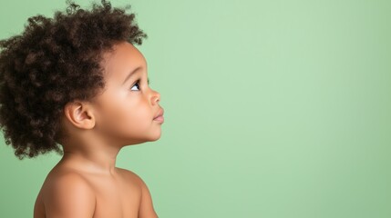 a profile of a young child looking upwards with an attentive expression on a mint-colored backdrop