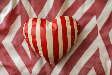 Obraz premium A plush red and white striped heart-shaped pillow on a bed, ideal for romantic getaways or Valentine's Day decorations