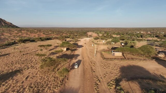 Aerial view of a matatu driving on a dusty dirt road through the serene savannah landscape, Wamba, Samburu, Kenya.