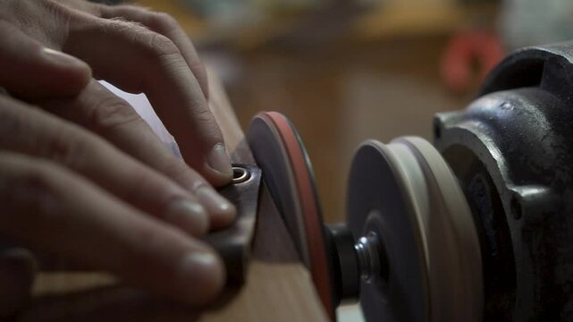 The tanner, with the help of machines for grinding, polishes the edges of leather goods. Close-up. Flying leather shavings