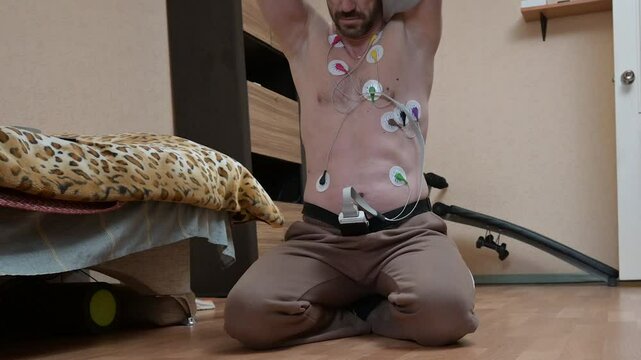 Man undergoing ECG/EKG cardiac monitoring at home with electrode patches on chest. Medical heart rhythm monitoring with electrocardiogram sensors. Holter monitor testing for heart health assessment.