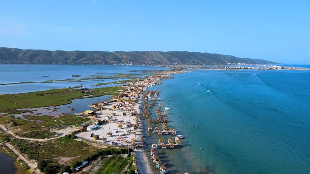 A panoramic view of Ghar El Meleh Beach in Bizerte, showcasing its stunning coastline.The beach is flanked by lush greenery and distant mountains,with numerous straw huts and boats adding to the charm