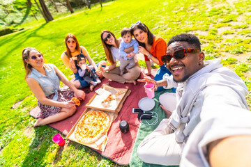 Happy friends taking selfie while enjoying pizza picnic at the park