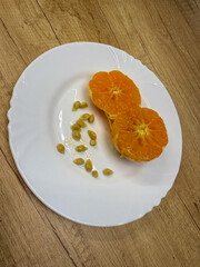 A halved mandarin with bright orange flesh and multiple seeds is placed on a white plate. The plate is placed on a wooden surface that contrasts with the color of the fruit.