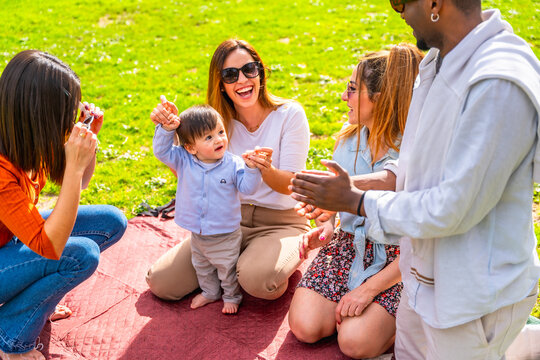 Happy multi ethnic family taking pictures and playing with baby boy in a park - Powered by Adobe