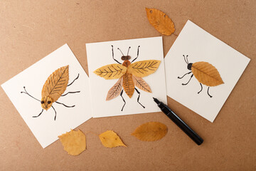 Handmade insect artwork using autumn leaves and black ink drawing on paper. Flat lay composition...