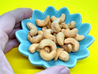 Cashew on small plate with hand close up.