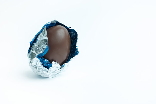 A partially unwrapped chocolate Easter egg with silver and blue foil on a white background. A festive and delicious treat, perfect for Easter promotions, food photography, and seasonal marketing.