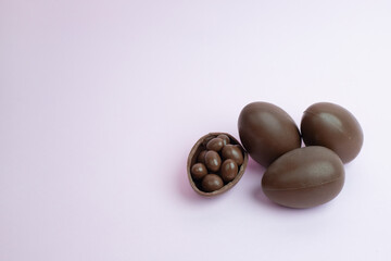 Four chocolate Easter eggs on a soft pastel background, with one broken open revealing chocolate-covered candies inside. A delicious and festive image for seasonal promotions and sweet treats.
