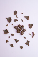 Overhead image of chocolate candies and broken chocolate egg shells artistically arranged on a smooth pink pastel backdrop, ideal for concepts involving sweets or Easter