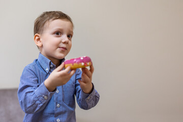 Smiling boy holding a pink frosted donut. A cheerful young boy in a blue shirt holds a pink frosted...