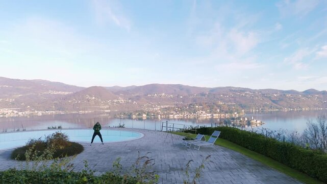 Man Flying Drone On Poolside With View Of Lake Orta In Pella, Novara, Italy. FPV shot