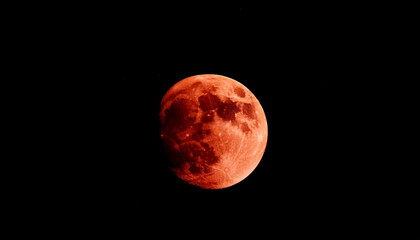Dramatic eclipsed moon with deep reddish hue against black sky.