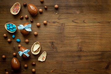 Top view of lots of chocolate Easter eggs with blue ribbon on a wooden background