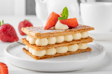 French dessert millefeuille with vanilla cream and fresh strawberries on a white plate on a white...