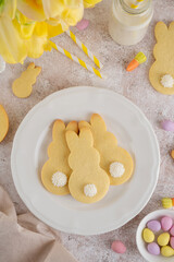 Easter Bunnies cookies on a white plate on a concrete background with flowers. Easter food background. Top view, copy space.