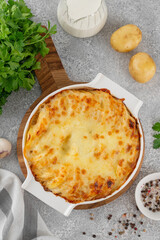 Potato gratin with cream, cheese and garlic in a white ceramic form on a gray concrete background. Potato casserole. Top view, copy space.