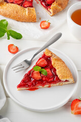 Galette, open pie or tart with strawberries with cup of tea on a white wooden table. Summer sweet pie.