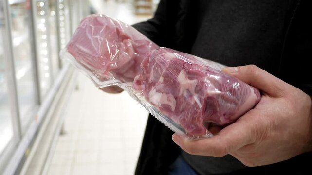 Human hands holding packaged fresh meat fillets, choosing turkey for cooking in supermarket, butcher's shelves