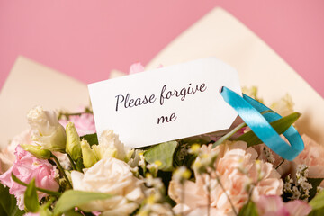 apology bouquet with a heartfelt "please forgive me" card attached by a blue ribbon, featuring delicate pastel flowers on a soft pink background
