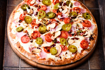Pizza with ham, cherry tomatoes and mozzarella cheese. Wooden background. Soft focus. Close up.