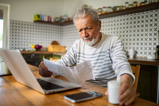 Senior man reading medication instructions while using laptop at home - Powered by Adobe