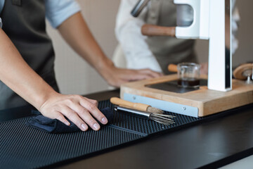 Entrepreneurship and Barista Skills. A focused barista meticulously cleaning the counter in a trendy coffee shop environment.