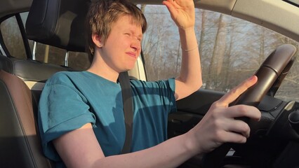 young woman with short haircut behind the wheel has problems with driving because of sun in eyes in...