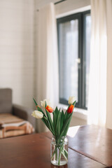 Bouquet of beautiful fresh tulips in a glass vase on wooden table in cozy modern interior. Spring flowers in glass vase at home.