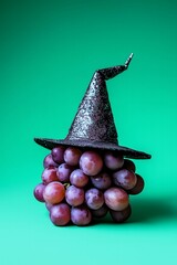Minimalistic dark grapes with a cute dark witch hat on a pastel green background. Halloween, cute, healthy concept.