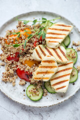 Grilled halloumi cheese with quinoa, bell pepper and cucumber served on a grey plate, vertical shot, middle close-up