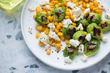 Roasted Brussels sprouts with corn and cottage cheese served on a white plate, close-up, horizontal shot, selective focus