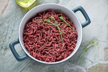 Raw beef mincemeat with seasonings in a grey serving tray, horizontal shot on a grey granite background, high angle view
