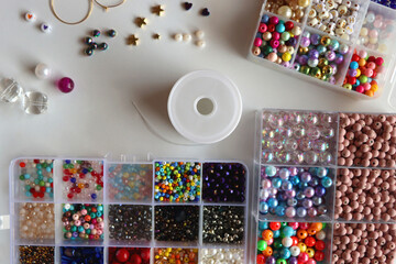 Hand figurine, colorful friendship bracelets, necklaces, various beads and DIY supplies on the table. Making jewelry at home. Flat lay.