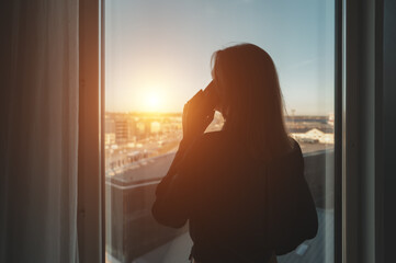 Silhouette of a woman talking on the phone by the office window.
