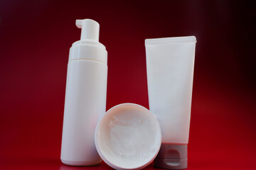 Creams in a jar and tube of white color, as well as foam for cleansing are close-up in the center on a pink background. The concept of body and face care, skin care, cosmetics. High quality photo